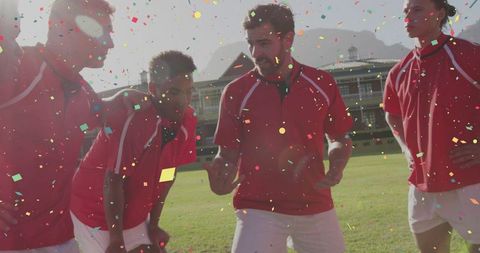 Red-jersey sports team huddling and celebrating with confetti on grass stadium field