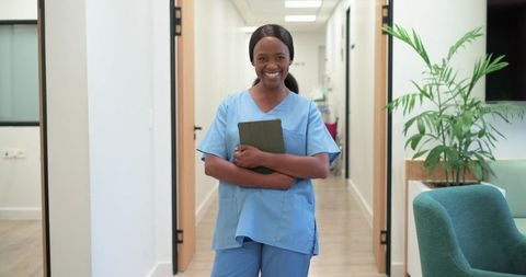 Smiling nurse standing in bright clinic corridor holding tablet welcoming patients