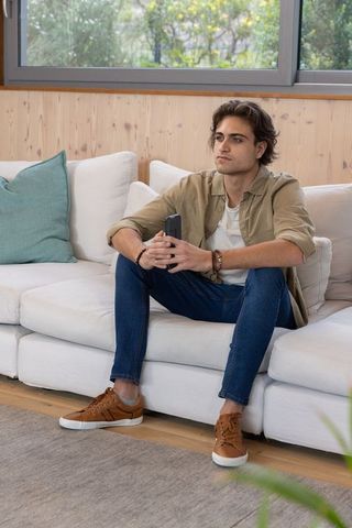 Relaxed Young Man Sitting on Sofa Holding Smartphone in Modern Living Room