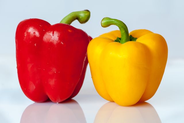 Red and yellow bell peppers placed next to each other on a white background. Showcasing vibrant colors and fresh texture, they are ideal for recipes, menus, and nutritional articles. This image can be used for blogs on health and wellness, grocery advertisements, and cookbooks to highlight fresh produce.