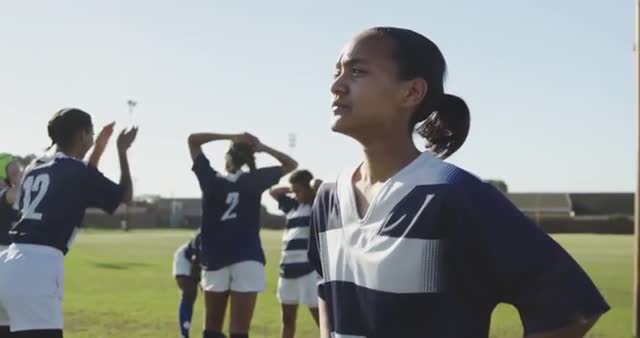 Rugby player standing on a field looking into the distance, showing focus and determination. Teammates are engaging in stretches in the background. Useful for promoting sportsmanship, teamwork, and the concept of being ready for competition. Ideal for sports advertisements, team building programs, or motivational content aimed at youth and athletics engagement.