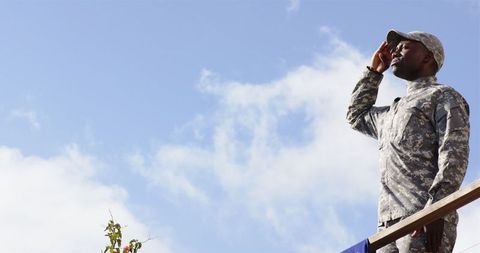 Military soldier saluting against blue sky