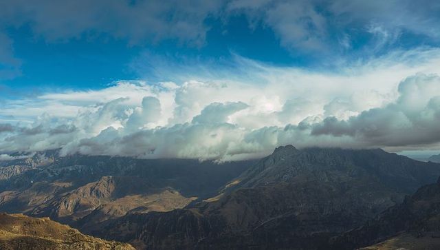 Jagged alpine peak rising through low cloud bank, sunlit ridges and dramatic sky panorama