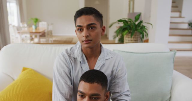 Smiling biracial gay male couple sitting in living room holding hands embracing and talking. staying at home in isolation during quarantine lockdown.