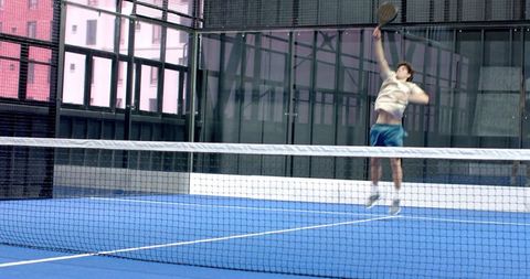 Male athlete jumping on blue padel court, striking ball in mid-air