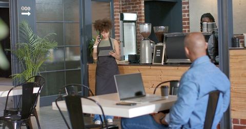 Urban coffee shop teamwork: african american barista chatting with customer, laptop on table