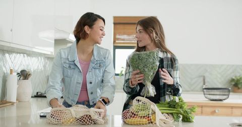 Women unpacking groceries with reusable mesh produce bags at modern kitchen island