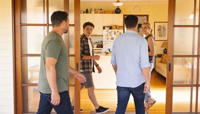 Friends entering sunny open-plan home through sliding wooden doors during casual gathering