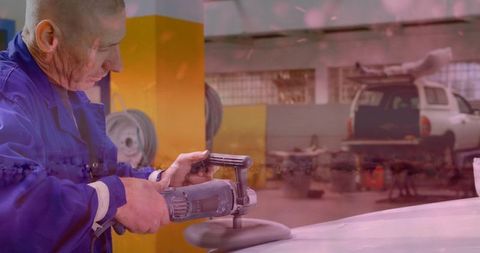 Mechanic in blue coverall buffing car hood in auto garage