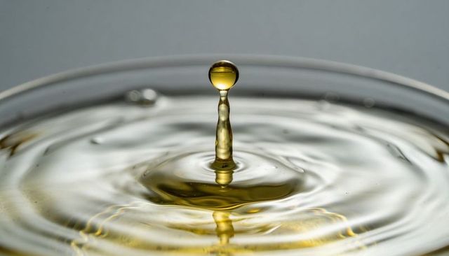 Golden droplet rising on slender liquid column with concentric ripples and reflective surface
