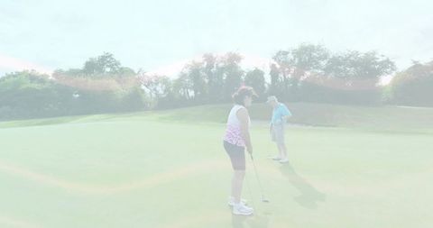 Woman lining up putt while partner watches on sunlit putting green with lens flare