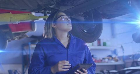 Female Technician Inspecting Car Undercarriage With Tablet in Workshop