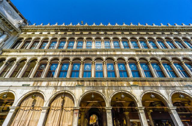 This photo captures the facade of the historic Rialto Building in Venice, showcasing its arched windows and classical architecture under a clear blue sky. Ideal for content related to travel, Italian culture, tourism, historical buildings, and European landmarks. Can be used in articles, travel guides, and promotional materials for Italy and Venice.