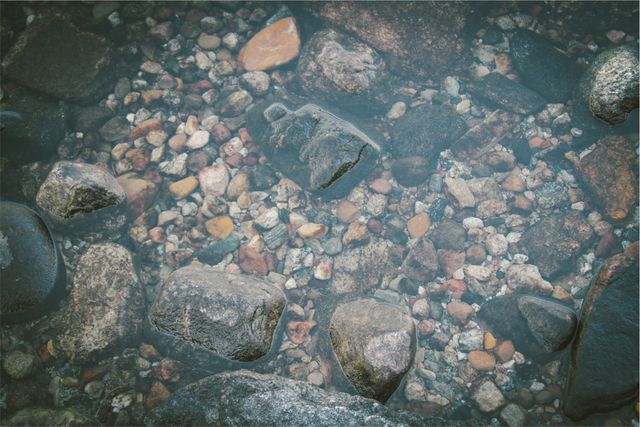 Crystal clear shallow water revealing smooth pebbles and rocks beneath the surface. Ideal for use in environmental campaigns, nature blogs, meditation media, or as a serene background image.