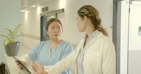 Doctor and nurse discussing patient information at hospital nurse station using tablet