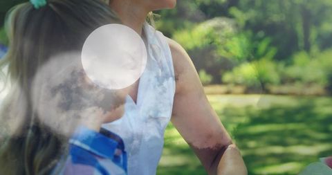 Mother sitting two children leaning close in sunlit park double exposure lens flare bokeh