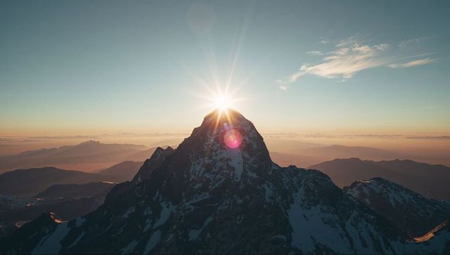 Sunrise Illuminating Snow-Dusted Mountain Peak with Flare