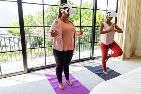 Women practicing virtual reality yoga in sunlit bedroom near balcony doors