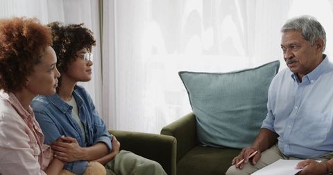 Senior man consulting adult family members while discussing paperwork on living room sofa