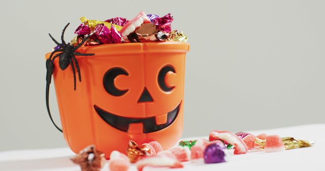 Scene of a Halloween pumpkin bucket filled with a variety of colorful candies, embracing Halloween spirit. Suitable for promoting Halloween events, advertising candy products, or enhancing festive decor ideas.