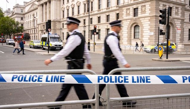 Uniformed police officers walking past police line tape outside historic government building
