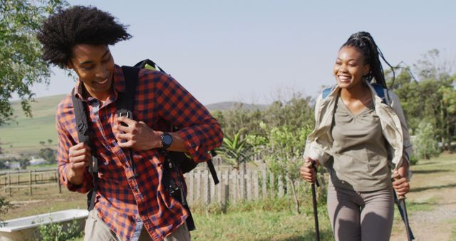 Happy african american couple with backpacks, hiking with trekking poles together, slow motion. Outdoor lifestyle, countryside and nature concept.