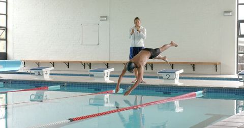 Swimming coach training young athlete indoor pool dive