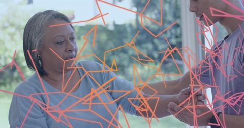 Caregiver helping senior woman near glass door with abstract geometric overlay