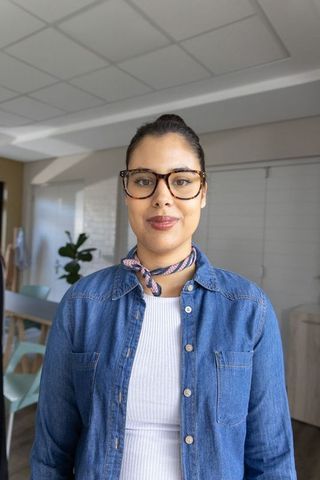 Confident woman in modern dining area wearing denim shirt and tortoiseshell glasses