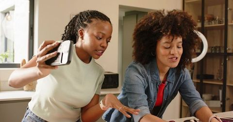 Diverse women creating social media content in kitchen using smartphone and ring light