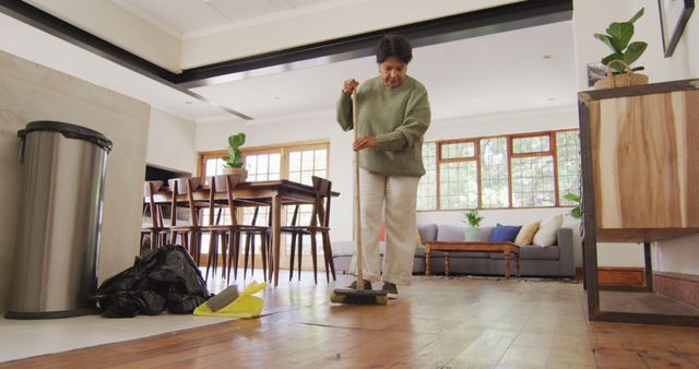 Senior woman cleaning hardwood floor in modern living room with wooden furniture. Ideal for content related to active seniors, home maintenance, and housekeeping routines.