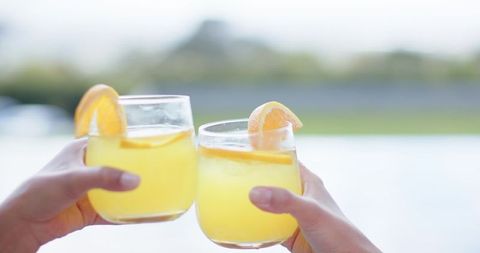 Diverse female friends clinking stemless glasses poolside with orange wedges