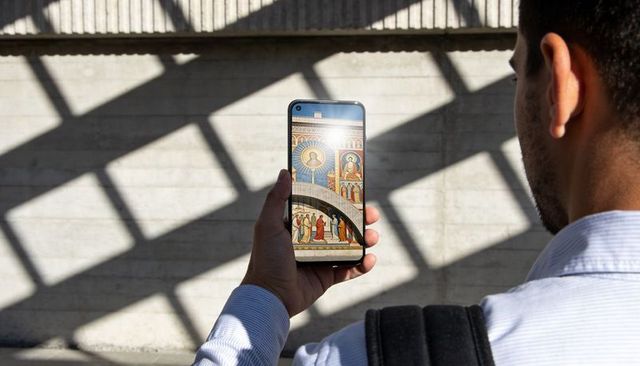 Man holding smartphone viewing colorful religious mosaic on device with geometric shadows