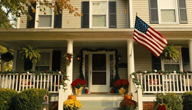 Welcoming autumn porch with american flag, wreath, pumpkins and festive garland
