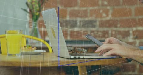 Man working remotely tapping smartphone at cafe table with laptop, sunglasses, orange juice