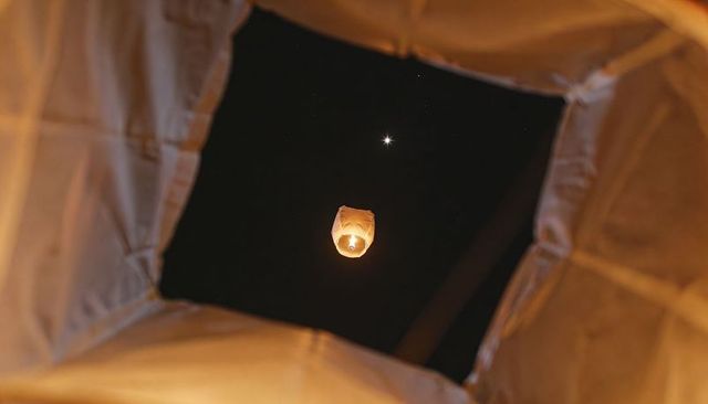 Sky lantern rising through square fabric frame at night with warm amber glow and star