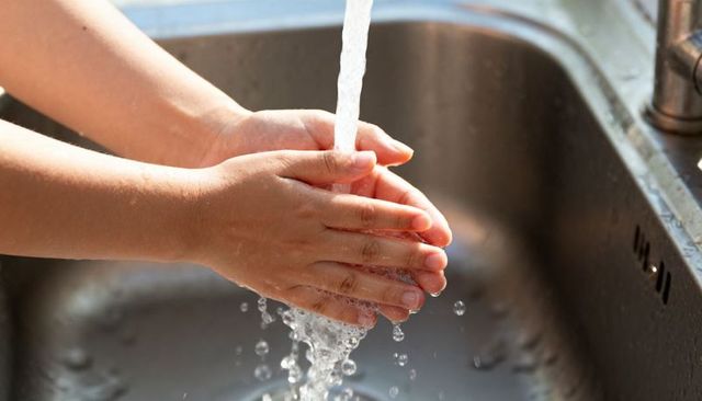 Child washing hands at kitchen sink under running faucet with water droplets closeup