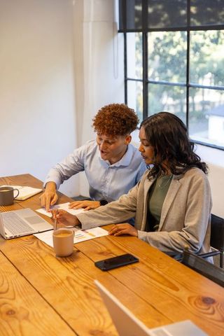 Collaborating coworkers analyzing charts and laptop at bright modern conference table