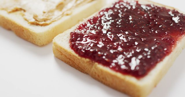 Two slices of white bread are shown close-up, one spread with peanut butter and the other with jelly. This can be used to illustrate snack preparation, breakfast ideas, or leafy afternoon indulgences. Suitable for use in culinary blogs, recipe websites, cooking articles, and food-related advertising.