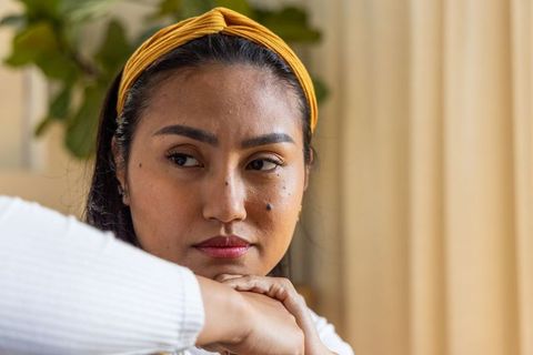 Contemplative asian woman resting chin on folded hands wearing mustard yellow headband