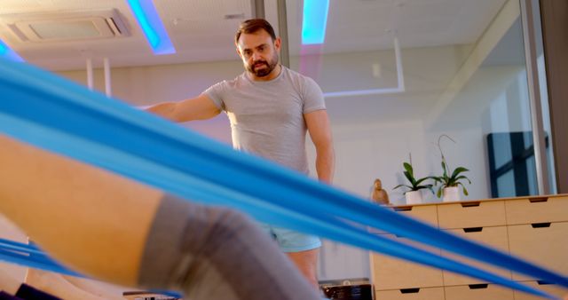 Fitness trainer assisting person during resistance band exercise in modern gym. Trainer supervises to ensure correct form and safety. Use for fitness programs, personal training promotions, or health and wellness content.