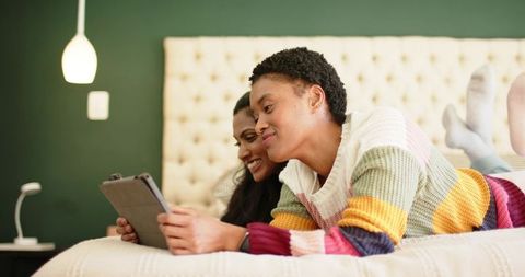 Diverse Friends Relax on Bed Browsing Tablet Together
