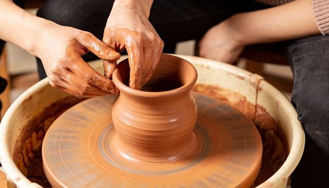 Hands shaping terracotta pot on spinning pottery wheel in ceramics workshop