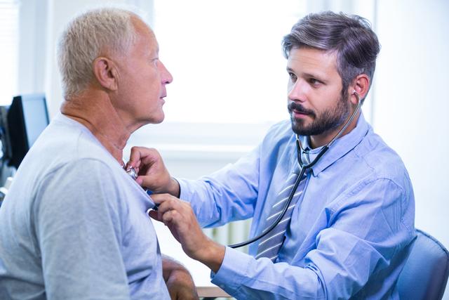 Male doctor conducting a medical examination on an elderly patient using a stethoscope in a medical office. Ideal for healthcare, medical services, senior care, doctor-patient relationship, and hospital-related content.