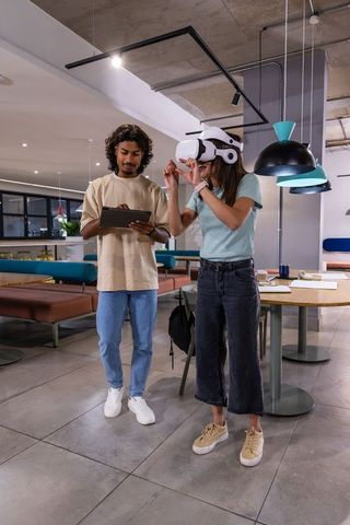 Indian man with tablet and colleague testing VR headset in modern coworking office