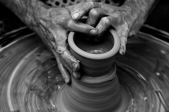 Hands are shaping a piece of clay on a spinning pottery wheel. The craftsmanship and artistic nature of pottery making are showcased, primarily suitable for websites or articles related to traditional crafts, artistic professions, and handmade goods. Fits well in educational content on pottery making or to illustrate skilled artisanal work.