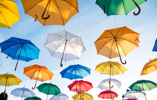 Photograph of multiple vibrant umbrellas floating or suspended against a clear blue sky. This image showcases urban art and creative decorative installations. Ideal for use in articles and websites about art installations, urban decoration, summer events, color schemes, outdoor creativity, and innovative design concepts.