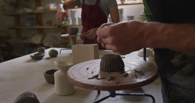 This image features artists shaping clay pots in a pottery studio, focusing on hands sculpting clay on a pottery wheel. This visual can be used for content related to creative arts, DIY crafts, pottery workshops, or artistic techniques in ceramic art.