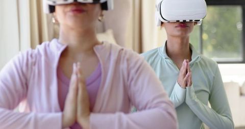 Multicultural women practicing virtual reality meditation at home with white vr headsets