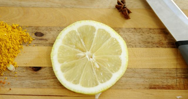 A sliced lemon sits next to a pile of spices and a knife on a wooden cutting board, with copy space. Its vibrant yellow adds a fresh, zesty appeal to the image, suggesting cooking or food preparation.